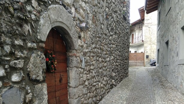 A narrow cobblestone street with a stone building featuring a wooden door and a small archway. - Lake Iseo in Esmate:The House of Fairies CIR.016200CNI00013 CIN IT016200C2UAHS6HFE (Solto Collina)