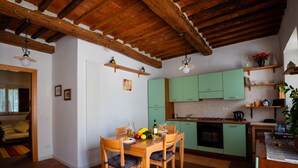 Uma cozinha compacta com armários verdes, uma mesa de jantar com cadeiras e teto de madeira.