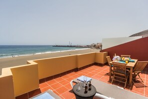A terrace with a view of the beach, a table with chairs, and a small round table with bottles and glasses. - Ocean View Penthouse II. Beachfront Wifi & A / C. 23m2 private terrace. (Gran Tarajal)