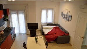 Une pièce compacte comprenant un coin cuisine, un lit avec une couverture rouge, une télévision et un coin repas avec une table et des chaises.
