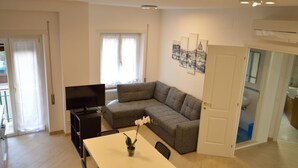 Un salon moderne avec un canapé d’angle gris, un téléviseur à écran plat, une table à manger avec des chaises et un pot d’orchidée.