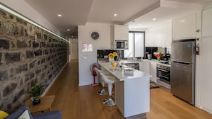 Una cocina moderna con una isla central, muebles blancos, una pared de acento de piedra y un extintor visible.
