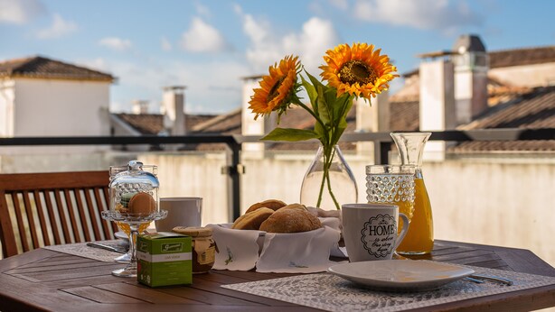 Una mesa dispuesta con una jarra de vidrio, una taza, un plato, una caja de galletas, un jarrón con girasoles y un frasco de vidrio.