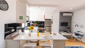 Una cocina moderna con armarios blancos, una isla central con asientos, un reloj y un televisor de pantalla plana.