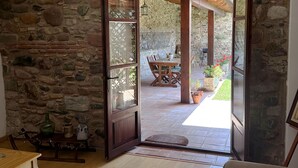 A cozy room with a stone wall, wooden ceiling, and a view of an outdoor patio with a table and chairs.