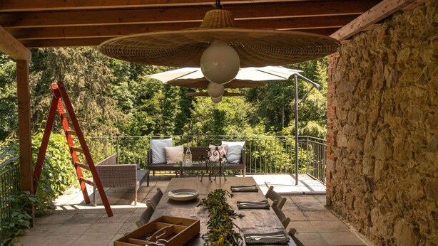 Een terras buiten met een houten eettafel, rieten meubels en een decoratieve plantenpresentatie.