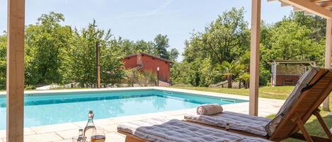 Zona de piscina con una silla de descanso y una mesa con una bandeja de bebidas y vasos.