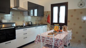 A kitchen with a stove, sink, and cabinets. There is a window with lace curtains and a clock on the wall. - Apartment in villa with garden CIN IT032003C2BP5JM2B2 (Muggia (TS))