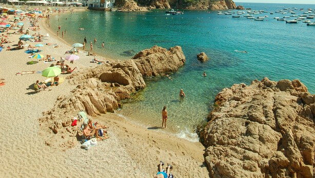 A beach with clear blue water, rocky formations, and buildings in the background. - Luxury, self contained, airconditioned studio with private terrace & use of pool (Begur)