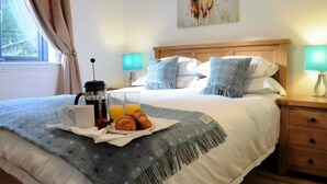 Ein ordentlich bezogenes Bett mit einer blauen Decke, ein Nachttisch mit einer Lampe und ein Fenster mit Vorhängen.
