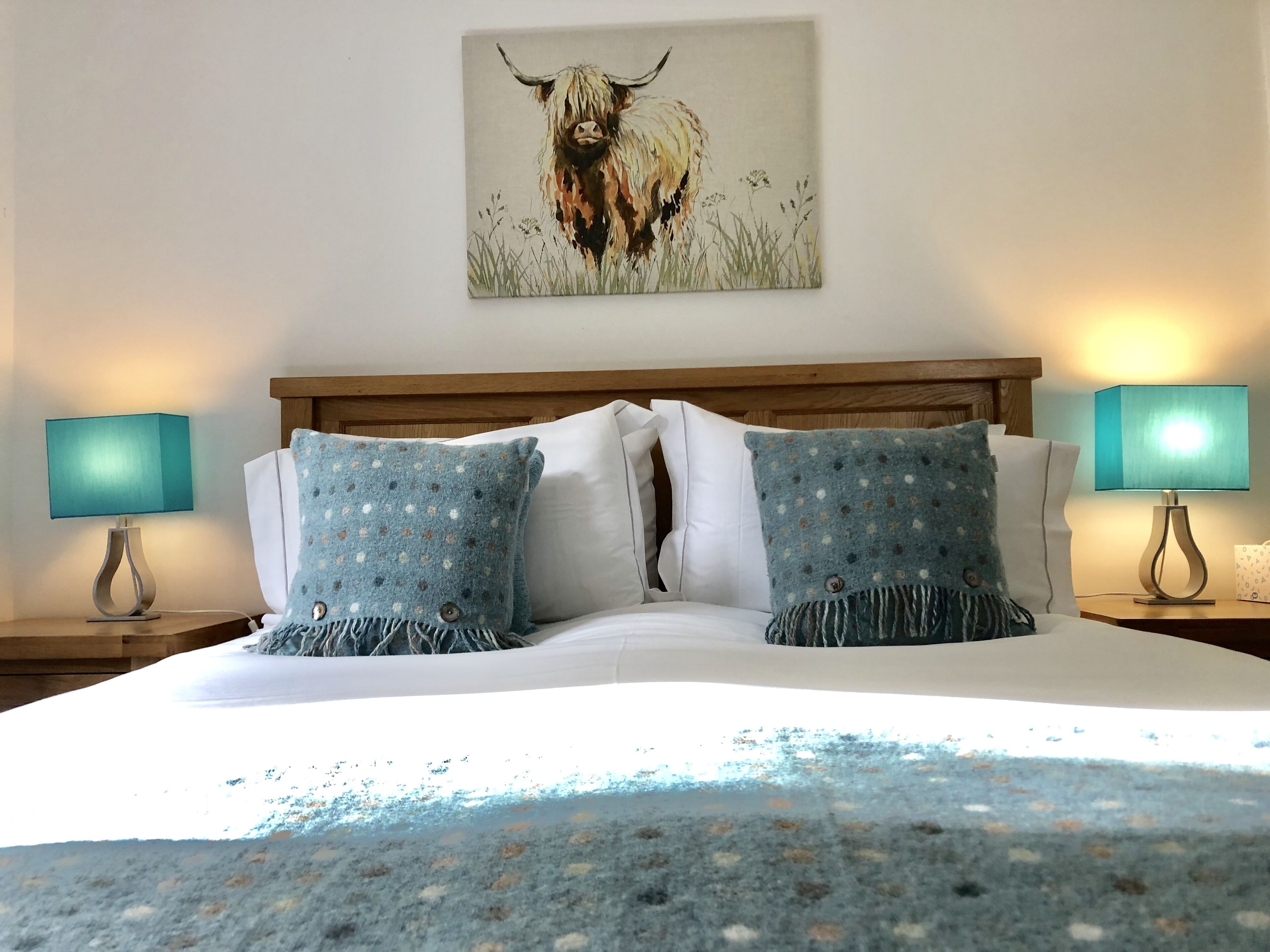 A bed with two pillows, a wooden headboard, and a painting of a bull on the wall.