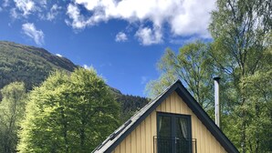 Eine Holzhütte mit einem Balkon, umgeben von Bäumen und einem Berg im Hintergrund.