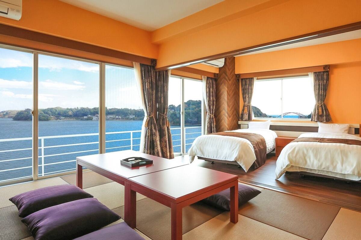 Een hotelkamer met twee bedden, een tafel en uitzicht op een wateroppervlak.