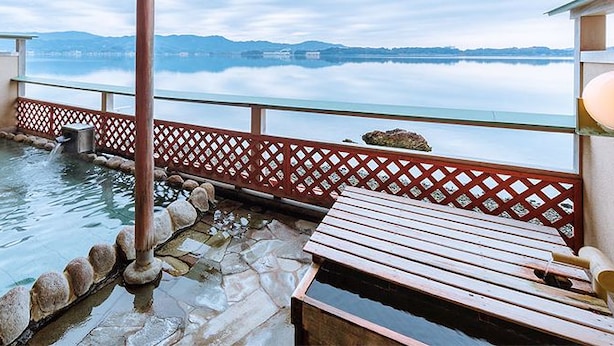 Un bain thermal avec un banc en bois, une bordure en pierre et une vue sur un lac et des montagnes.