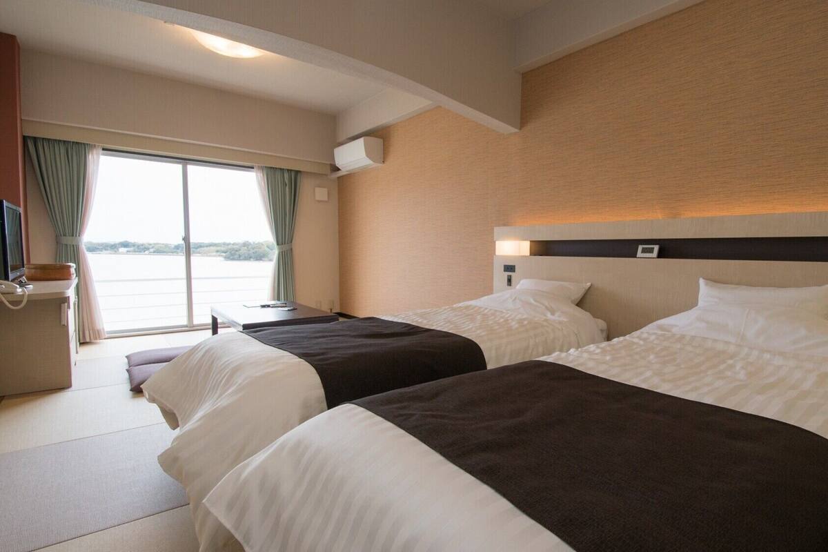 Een hotelkamer met twee bedden, een bureau, een stoel, een televisie en een raam met gordijnen.