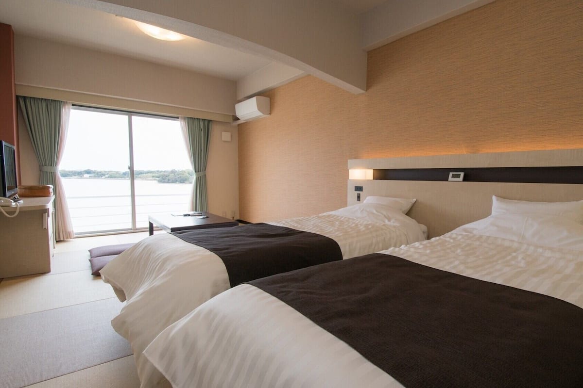 Habitación de hotel con dos camas, un escritorio, una silla, un televisor y una ventana con cortinas.