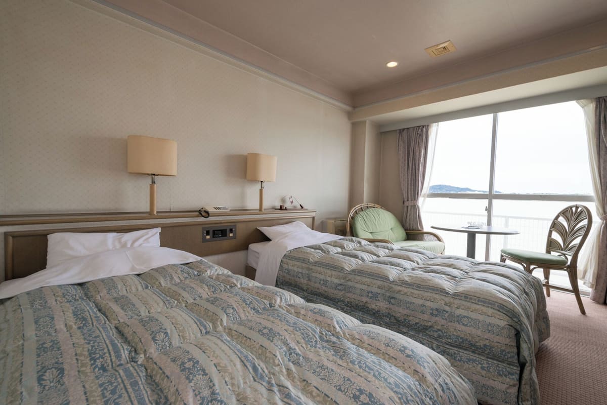 Een hotelkamer met twee bedden, een tafeltje, een stoel en uitzicht op zee.