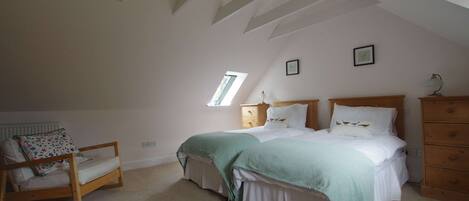A bedroom with a sloped ceiling, a bed with a green blanket, a wooden rocking chair, and a dresser.
