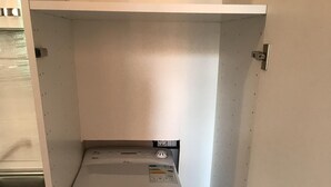 En kompakt tvätt- och torkmaskin som är installerad på en liten yta och har en metalldörr samt en liten hylla ovanför.