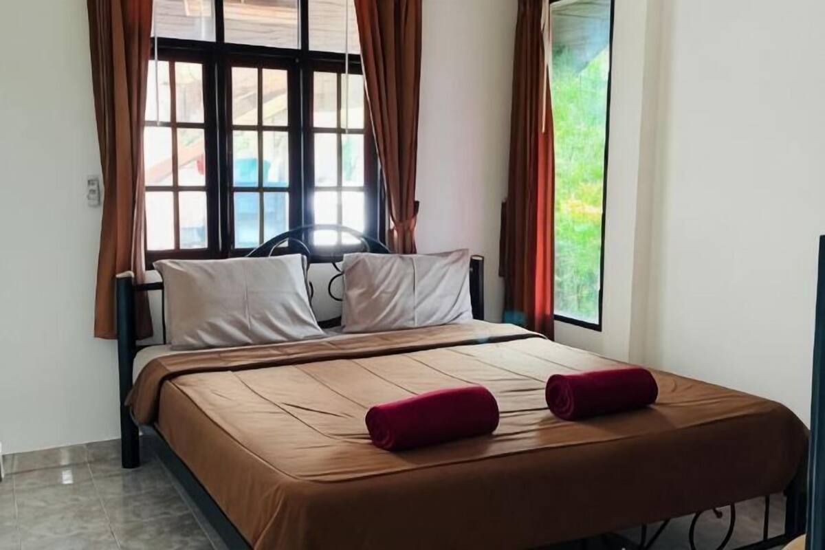 A bed with a brown cover, two pillows, and a red pillow on a metal frame.