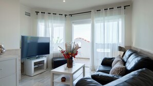 A modern living room with a flat-screen TV, a white coffee table, a black leather sofa, and a vase with flowers. - A UNIQUE PARADISE in Royal Beach, Mijas beach (Calahonda - Mijas Costa)