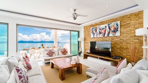 A modern living room with a large TV, white sofas, a wooden coffee table, and a view of the sea. - Luxury 5-bedroom villa with panoramic sea view (Koh Samui)