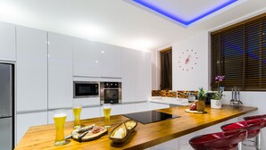 A modern kitchen with white cabinets, a wooden countertop, and red bar stools. - Luxury 5-bedroom villa with panoramic sea view (Koh Samui)