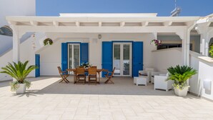 A covered outdoor patio with a wooden table and chairs, blue shutters, and potted plants. - Vacation Home Offers, Salento, Gallipoli-Torre San Giovanni di Ugento (Posto Rosso Alliste Marina)