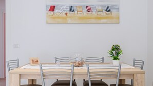 A dining area with a wooden table, metal chairs, a glass bowl with decorative items, a framed picture, and a potted plant. - Vacation Home Offers, Salento, Gallipoli-Torre San Giovanni di Ugento (Posto Rosso Alliste Marina)