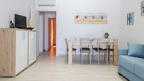 A modern living room with a dining area, a TV on a wooden cabinet, and a painting on the wall. - Vacation Home Offers, Salento, Gallipoli-Torre San Giovanni di Ugento (Posto Rosso Alliste Marina)