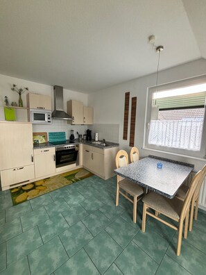 A compact kitchen with a dining area, a microwave, stove, and a window with curtains. - "Pearl of the Baltic Sea" - 2 room - Pearl of the Baltic Sea (Zinnowitz)