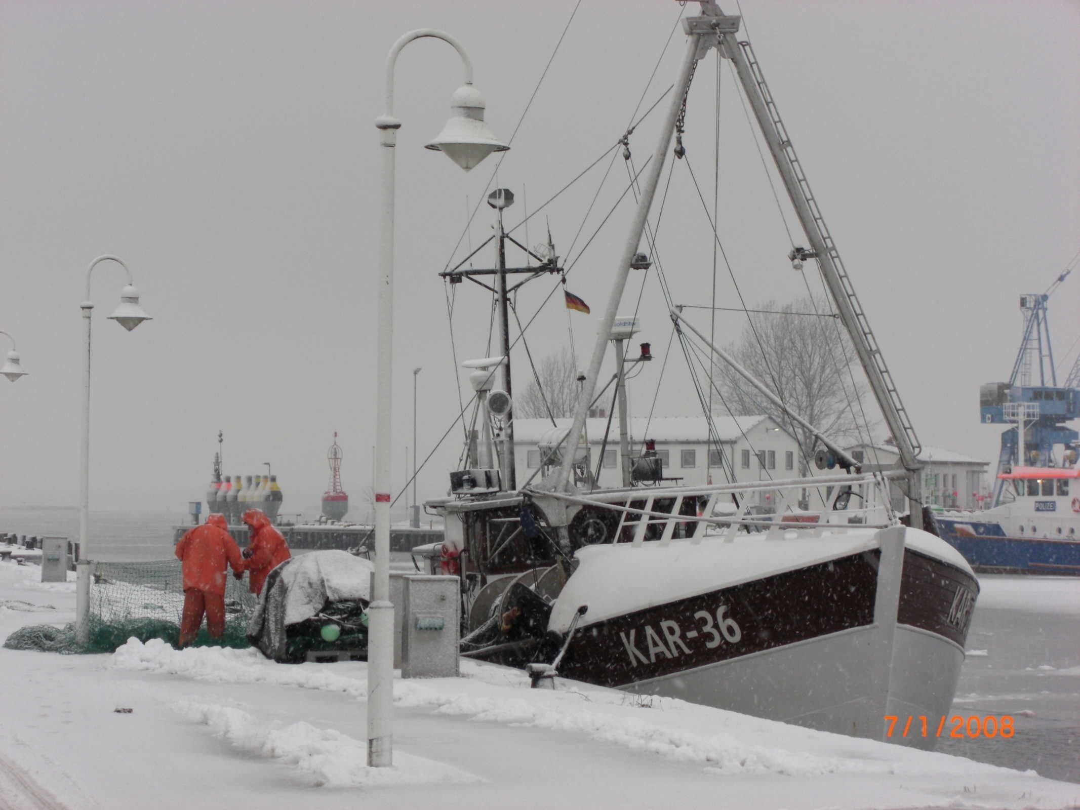 A boat named KAR-36 docked at a pier with snow on the ground and a cloudy sky.