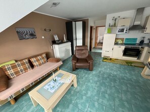 A living room with a sofa, a chair, a coffee table, and a kitchen area with cabinets and appliances. - "Pearl of the Baltic Sea" - 2 room - Pearl of the Baltic Sea (Zinnowitz)