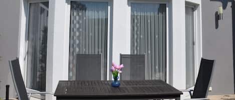 Een gebouw met twee verdiepingen, een balkon, grote ramen en een tafel met stoelen buiten.