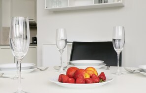 Une table à manger avec deux verres à vin vides, une assiette de fruits et de la vaisselle blanche.