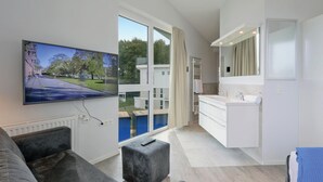 Um apartamento moderno com uma televisão grande, cozinha, banheiro e vista para um parque.