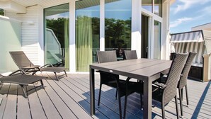 Eine überdachte Terrasse mit Tisch und Stühlen, großen Fenstern und Blick auf die Umgebung.