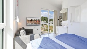 Ein Hotelzimmer mit Bett, einer Couch, einem Fernseher, einem Badezimmer und einem Balkon mit Blick auf Häuser.