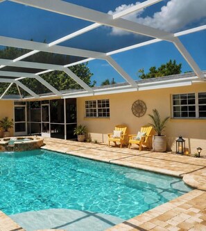 A swimming pool with a hot tub, surrounded by patio chairs and potted plants.