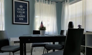 A room with a dining table, chairs, a framed sign, and a potted plant.