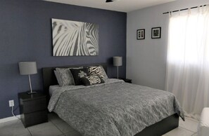 A bedroom with a bed, two nightstands, a wall-mounted zebra print artwork, and a window with curtains.
