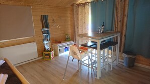 Een houten interieur met een eettafel, stoelen, een klein keukenhoekje en een raam met gordijnen.