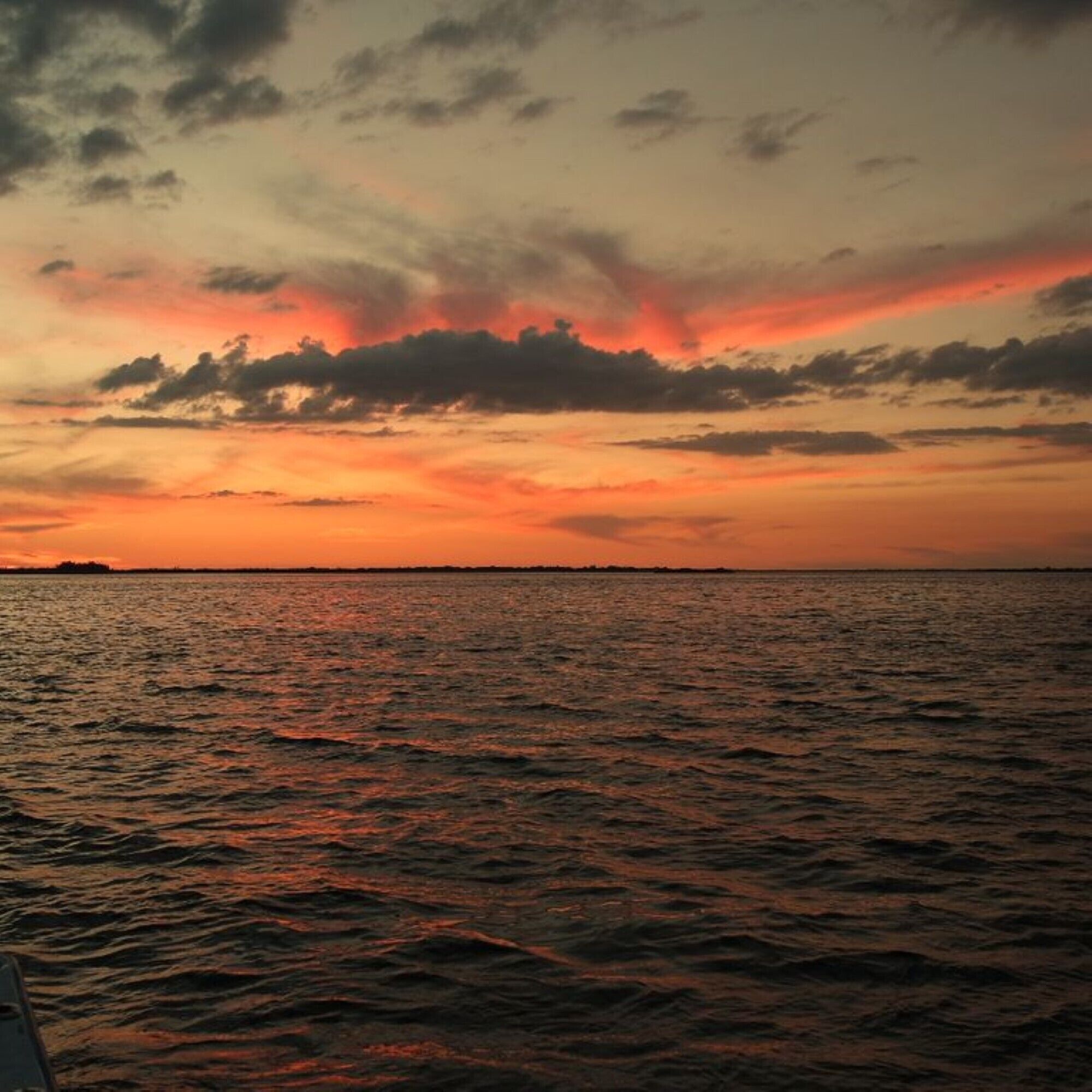 Un atardecer sobre un mar tranquilo con una costa lejana.