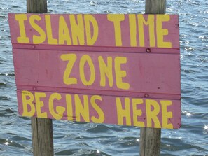 Une pancarte indiquant : « DÈBUT DU FUSÉAU HORAIRE DE L’ÎLE », avec en arrière-plan un paysage aquatique.
