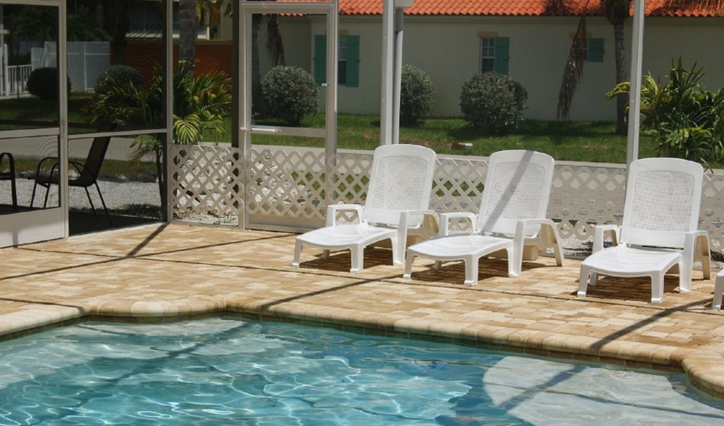 A swimming pool with four white lounge chairs and a view of a house with a red roof.
