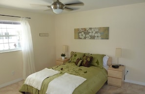 A bedroom with a bed, nightstands, a ceiling fan, a window with curtains, and a painting on the wall.