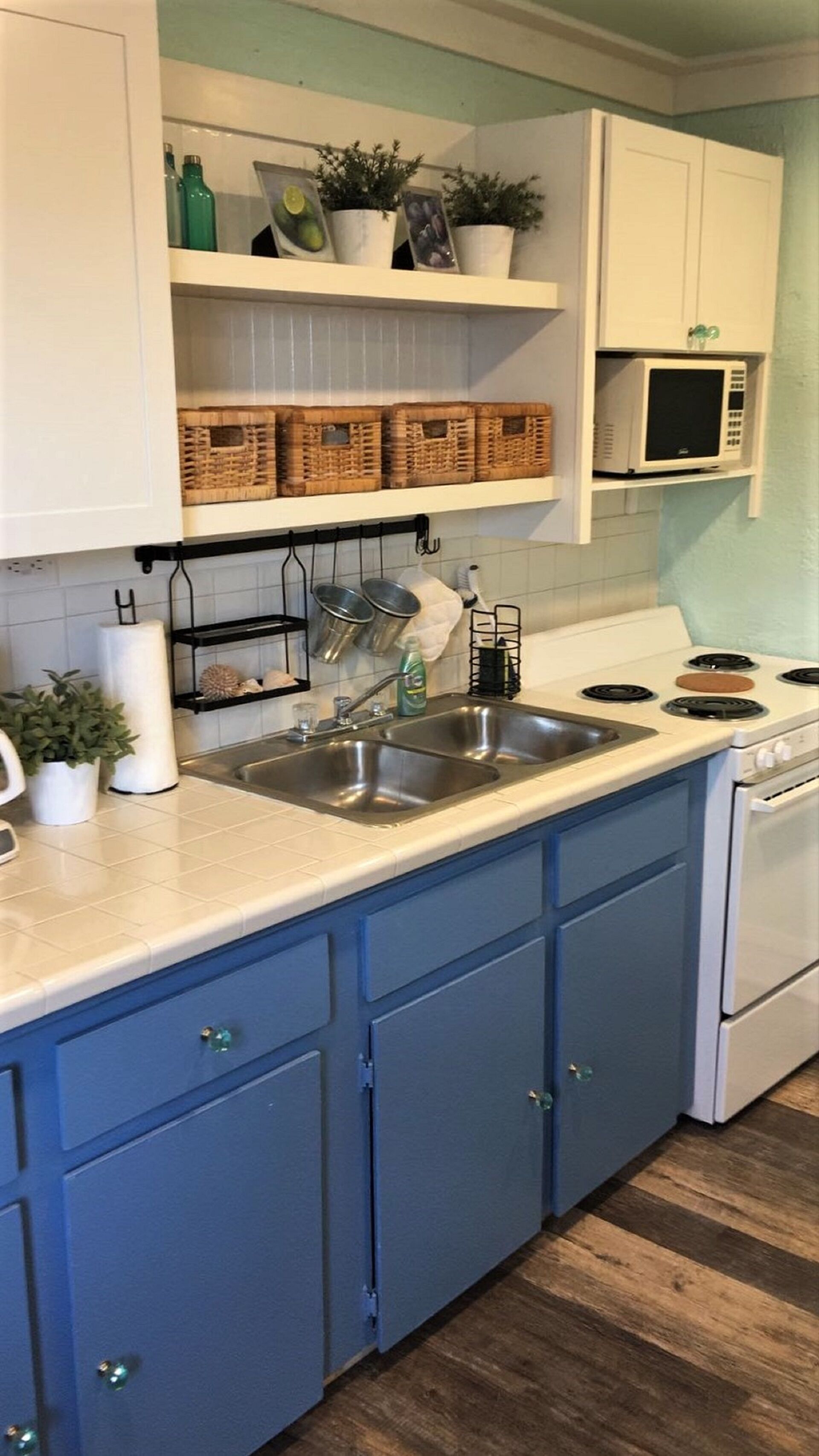 A kitchen with blue cabinets, a double sink, a stove, and a microwave.