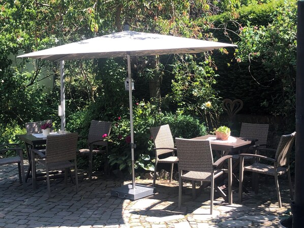 Eine Terrasse im Freien mit Tisch und Stühlen unter einer Markise, umgeben von üppigem Grün.