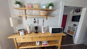 Un coin cuisine équipé d’étagères en bois, d’un four à micro-ondes, d’une machine à café et de divers ustensiles de cuisine.