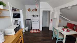 Une cuisine de taille modeste, avec des appareils électroménagers blancs, un ventilateur de plafond et un tapis à carreaux rouges.